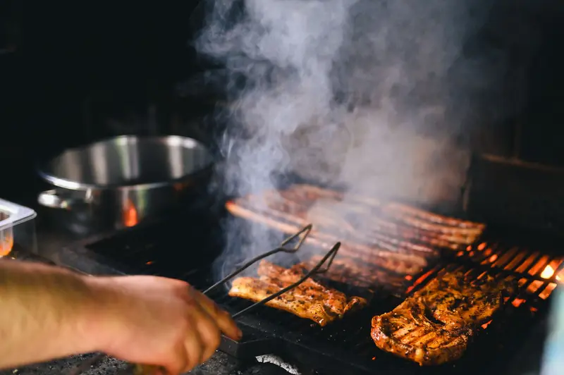 Close-up of grilling meat with smoke rising on a barbecue, outdoors
