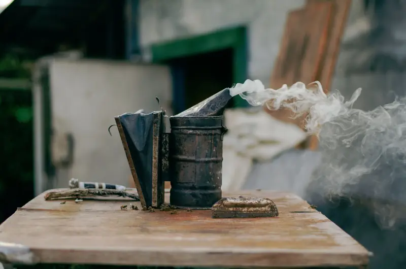 Close-up of a bee smoker releasing smoke on a wooden surface, outdoors