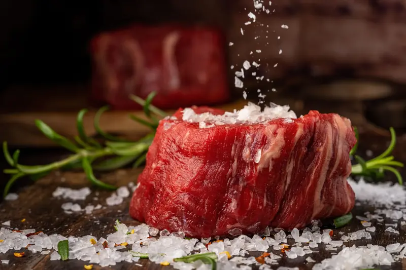 Close-up of raw beef steak with sea salt and herbs on a wooden surface