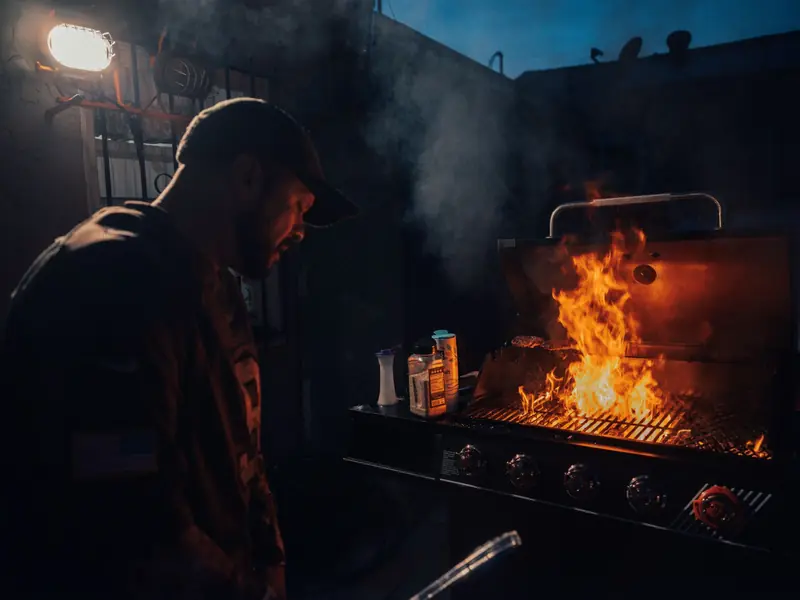 Man grilling barbecue on a flaming grill at night outdoors