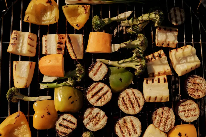 Assorted grilled vegetables including peppers, eggplant, and broccoli on a barbecue grill