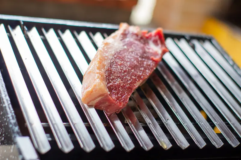 Close-up of a raw beef steak seasoned with salt on a grill grate in Recife, Brazil