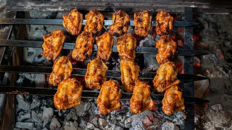 Juicy grilled chicken wings on skewers sizzling over a charcoal grill, perfect for a barbecue