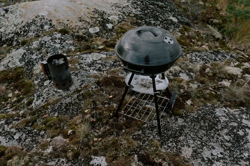 A metal grill and chimney starter on mossy rocks outdoors, perfect for camping BBQ