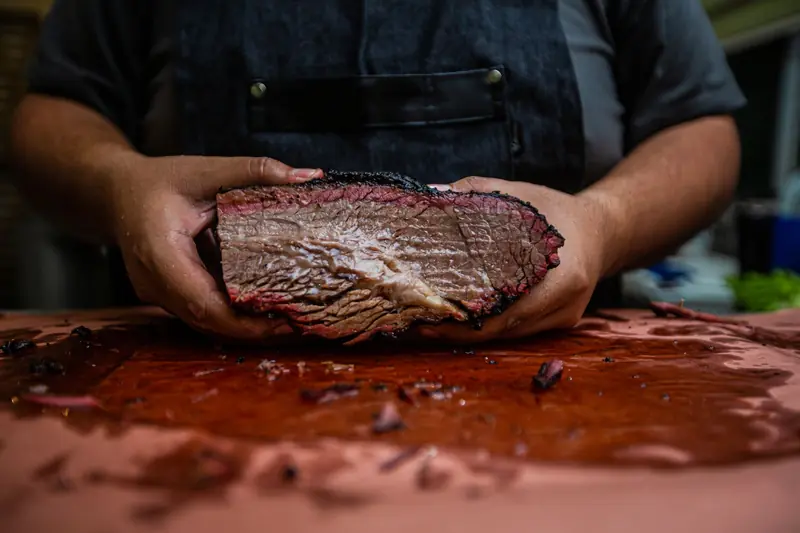 Close-up of a chef's hands holding a tender and juicy smoked brisket on a wooden board