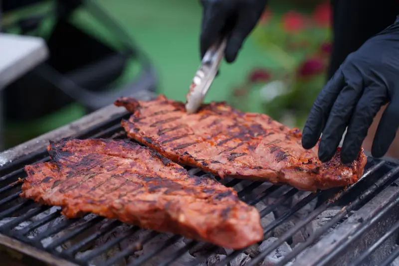 Close-up of juicy steaks grilling on an outdoor barbecue with gloved hands flipping meat