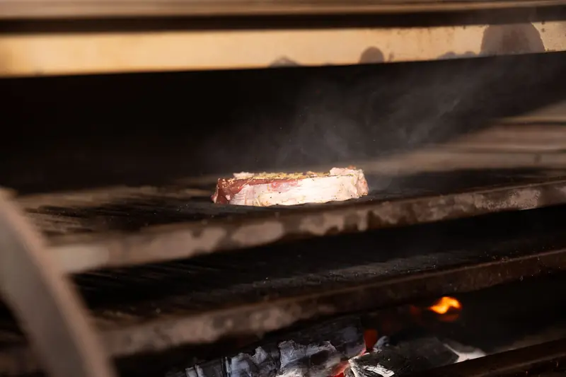 Close-up of a delicious steak cooking on a grill over an open flame, emitting smoke