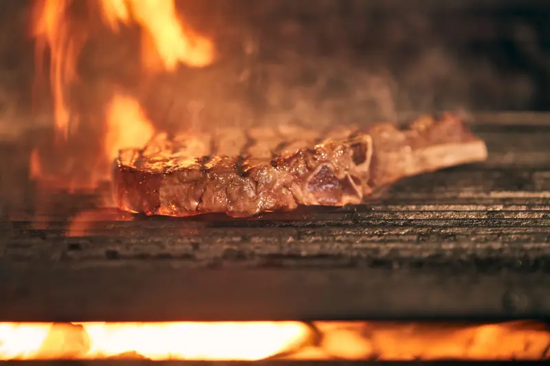 Juicy ribeye steak cooking over an open fire grill with flames, showcasing delicious grilling action