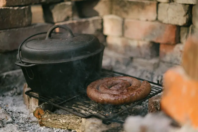Cast iron pot and sausage on grill outdoors in rustic setup