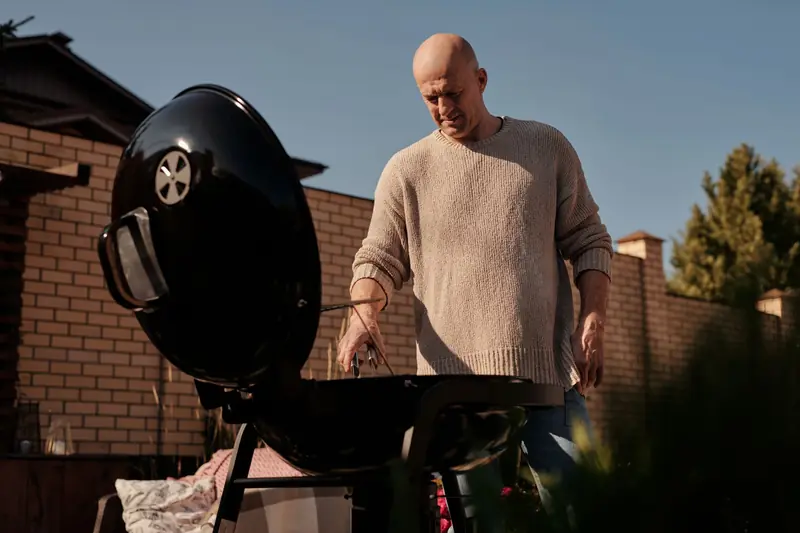 Man cooking on a barbecue grill outdoors, enjoying a sunny day in the backyard