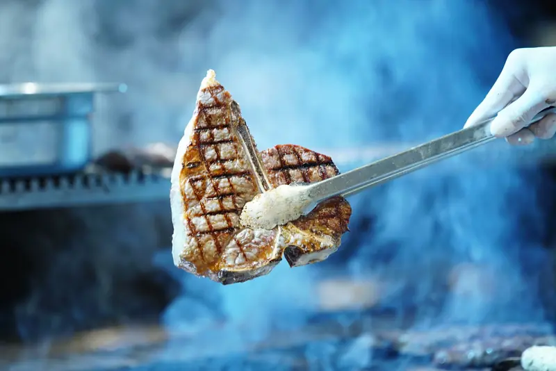 Delicious grilled steak lifted from the grill with tongs, smoky BBQ ambiance