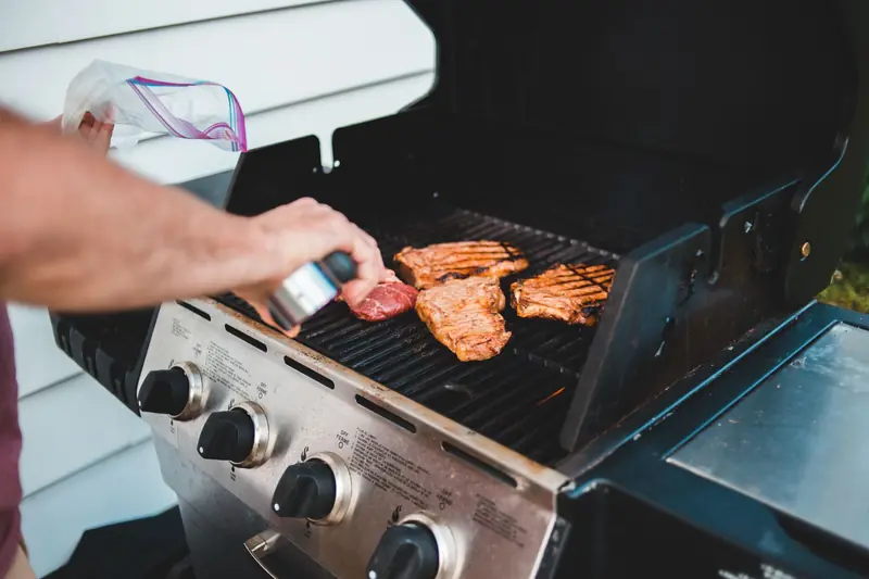 A man seasons steak on a grill for a backyard barbecue, displaying outdoor cooking