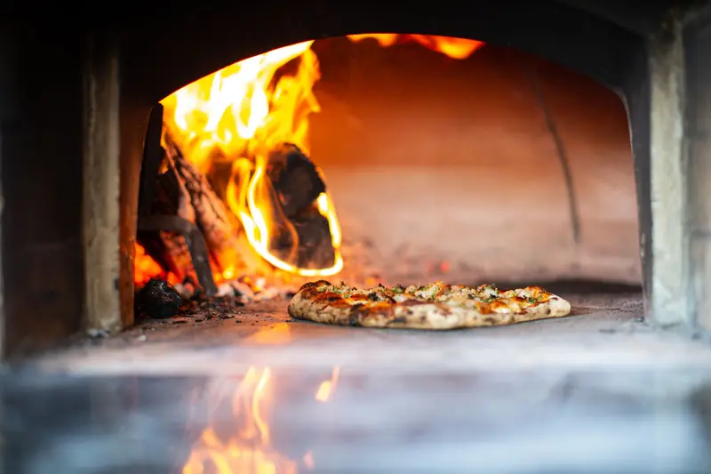 Delicious artisan pizza baking in a traditional wood-fired oven with flames