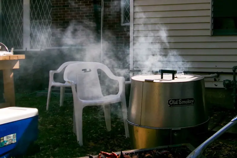 Smoke rising from a barbecue grill beside empty chairs in a Houston backyard setting