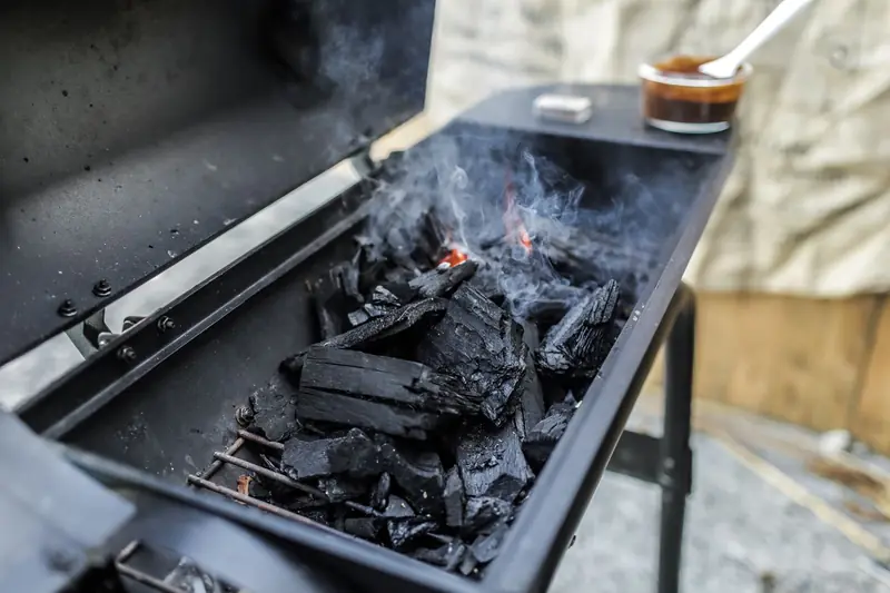 Close-up of a charcoal grill emitting smoke, showcasing burning coals and outdoor cooking setup