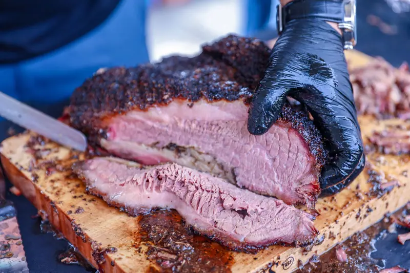 Deliciously smoked brisket being sliced with gloves on a wooden board