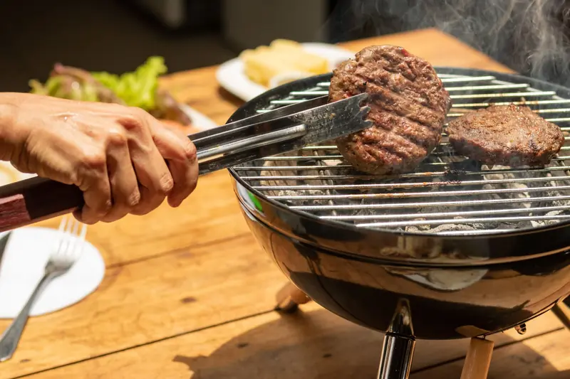 A hand uses tongs to grill burgers on a charcoal barbecue. Perfect for outdoor dining scenes