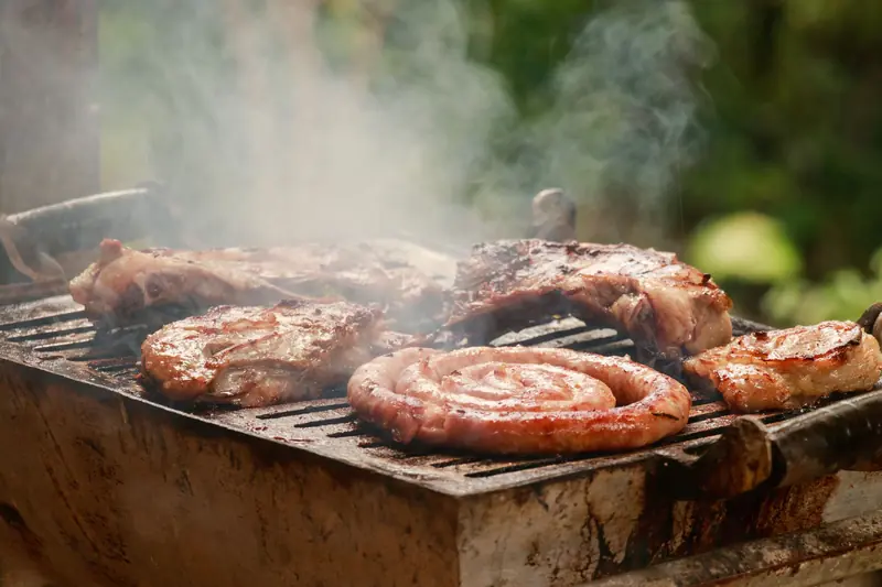 A sizzling BBQ grill with meat and sausages smoking outdoors, perfect for summer cookouts