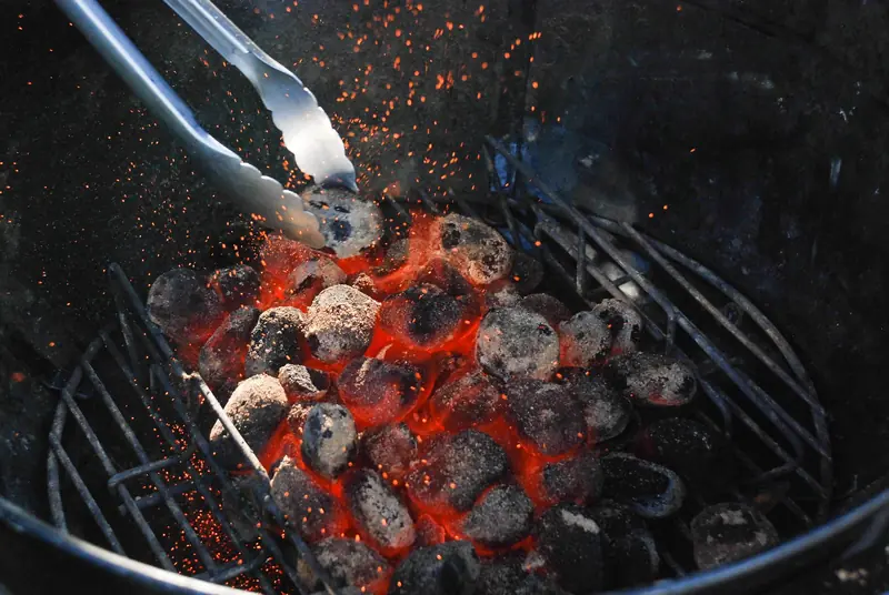 Close-up of hot, glowing charcoal briquettes in a grill, with tongs stirring embers