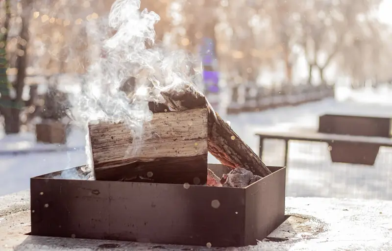 A cozy winter bonfire with smoking wood outdoors, surrounded by snowy scenery